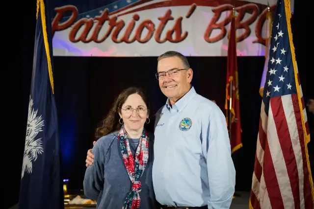 Two guests pose under the Patriots' BBQ banner