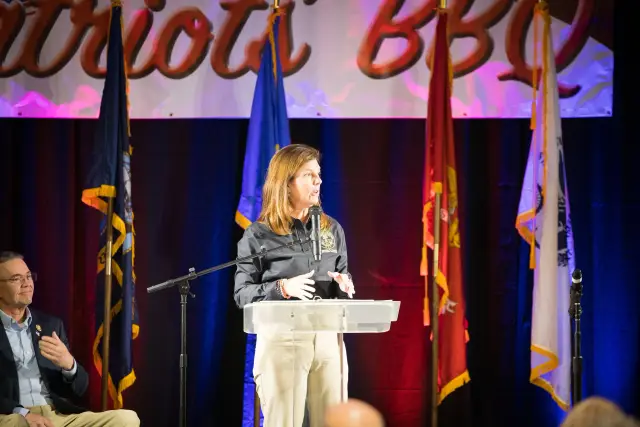A woman speaks at the podium in front of the flags