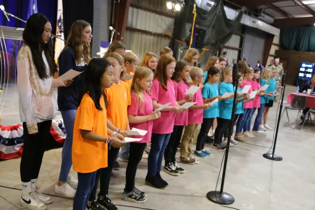 A children's choir in colored T-shirts sings from song sheets