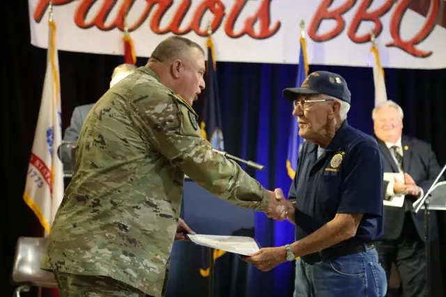 A soldier shakes hands with a veteran and hands him a certificate