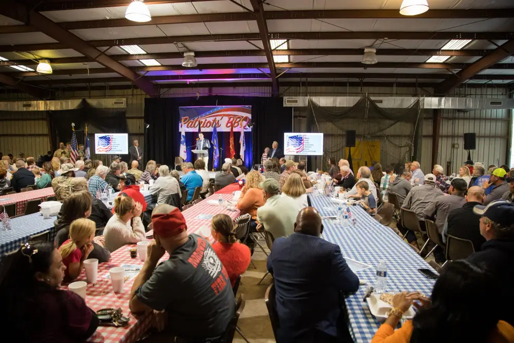 Guests at long tables facing the stage under the Patriots' BBQ banner at a past event